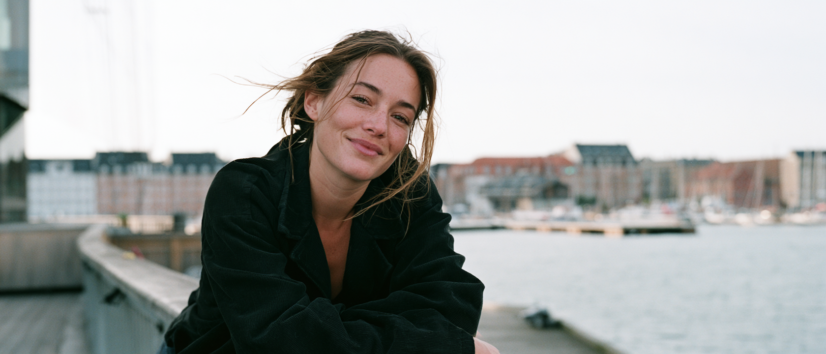 Smiling woman leaning on a railing beside a city waterfront